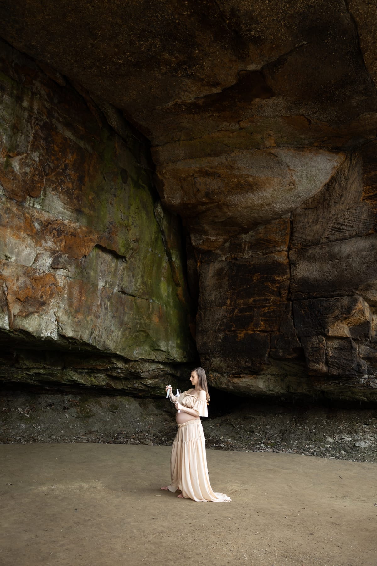 Katie, expecting, in a flowing dress beneath a vast cave arch