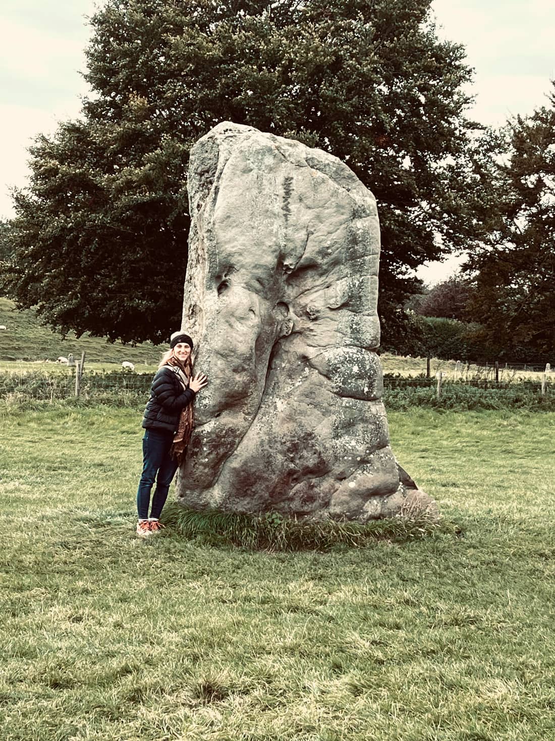 Katie resting a hand on an ancient standing stone in a green field